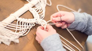 Hands knotting rope for macramé on table.