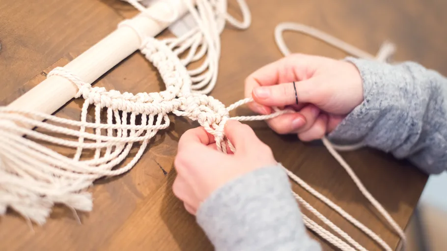 Hands knotting rope for macramé on table.