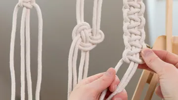 Hands knotting white macramé cords.