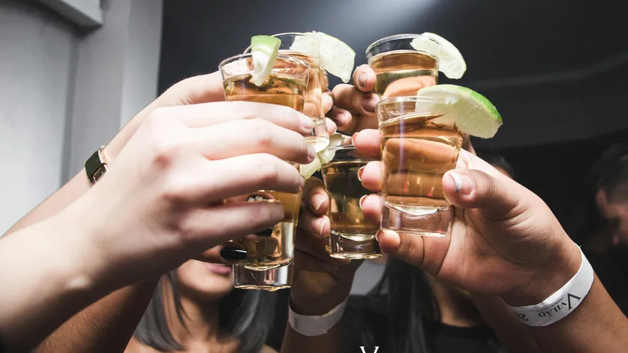 Hands hold shot glasses with lime slices.