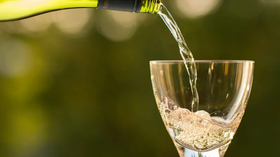 White wine pouring into glass, green background.