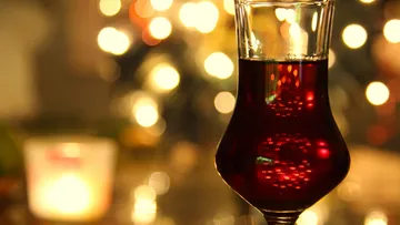 Weinglas mit roter Flüssigkeit, verschwommener Bokeh-Hintergrund.