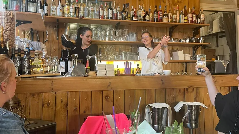 Two women making cocktails behind a bar.