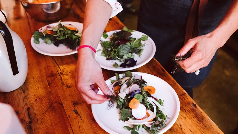 Person plating fresh salad on wooden table.