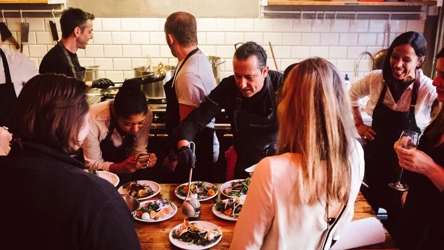 People gathered around chef plating dishes in kitchen.