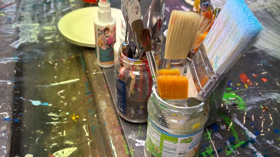 Paintbrushes in jars on a colorful table.
