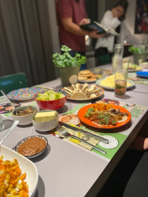 Tisch mit vielfältigem Essen, Personen stehen daneben.