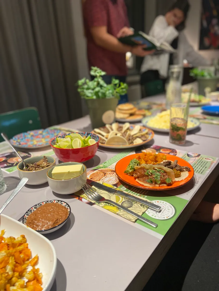 Tisch mit vielfältigem Essen, Personen stehen daneben.