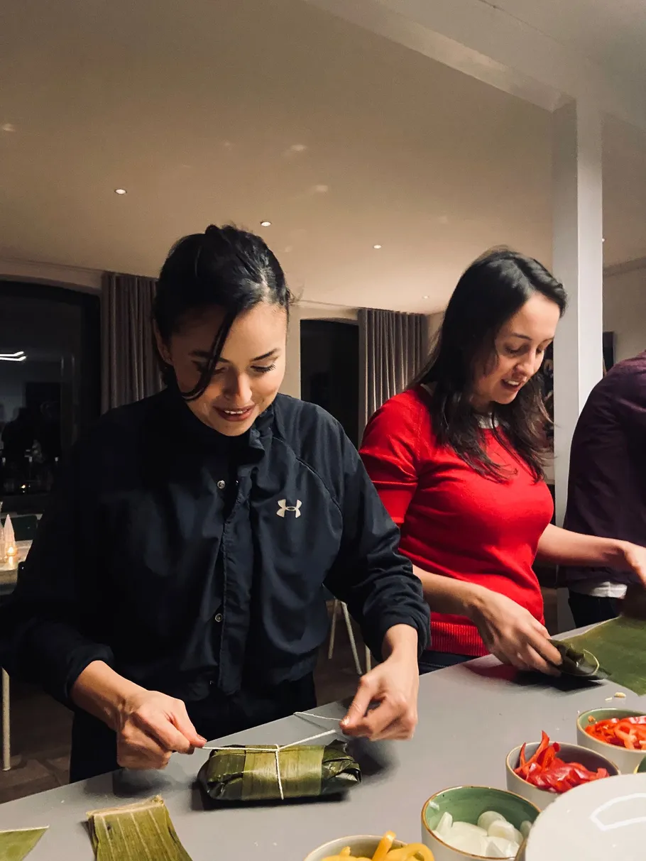 People wrapping food in leaves at kitchen table.