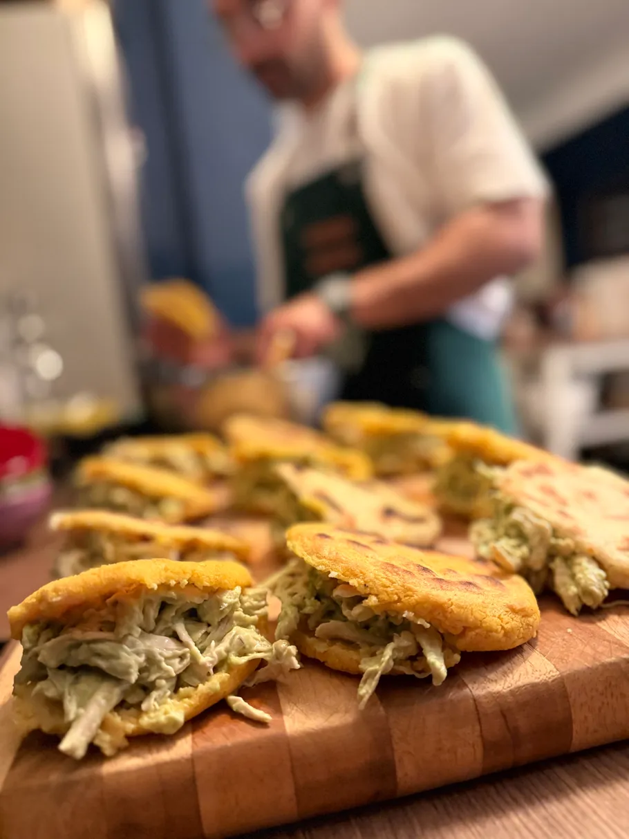 Arepas with filling on wooden board, chef in background.