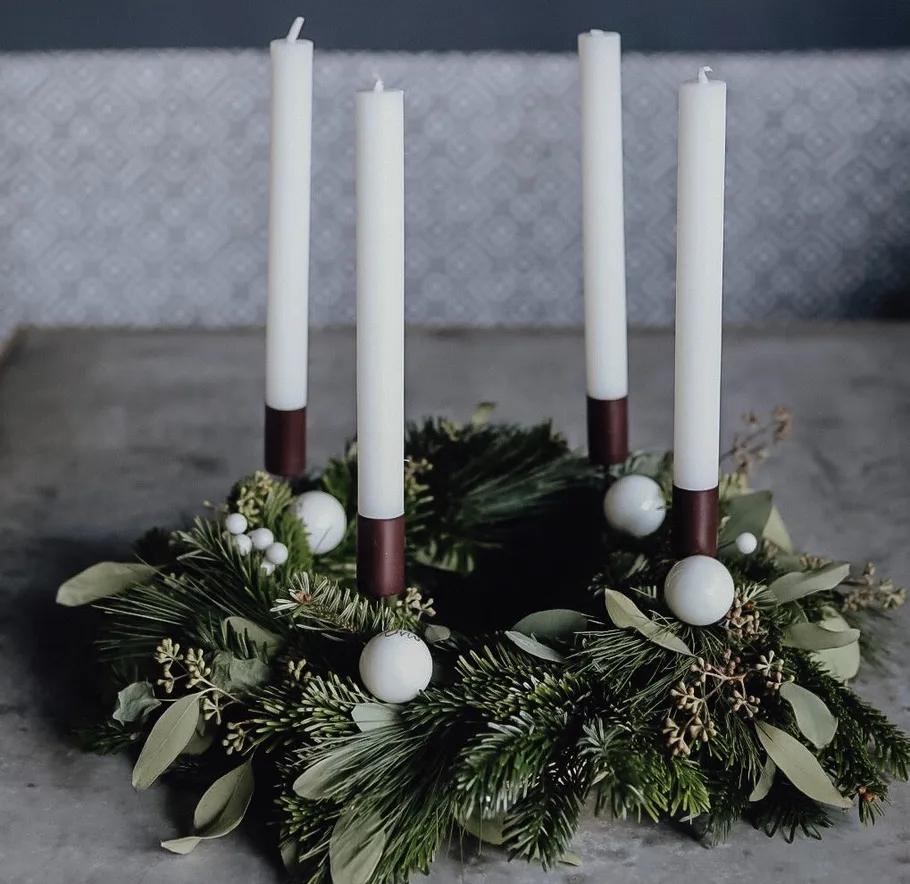 Four candles in decorative wreath on table.