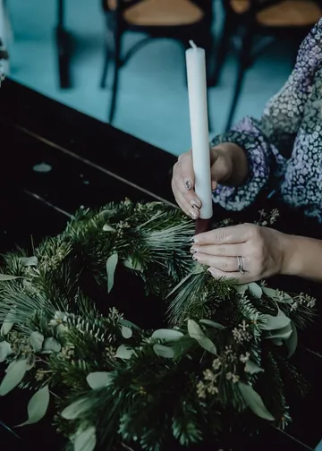 Person arranging candle on festive wreath.