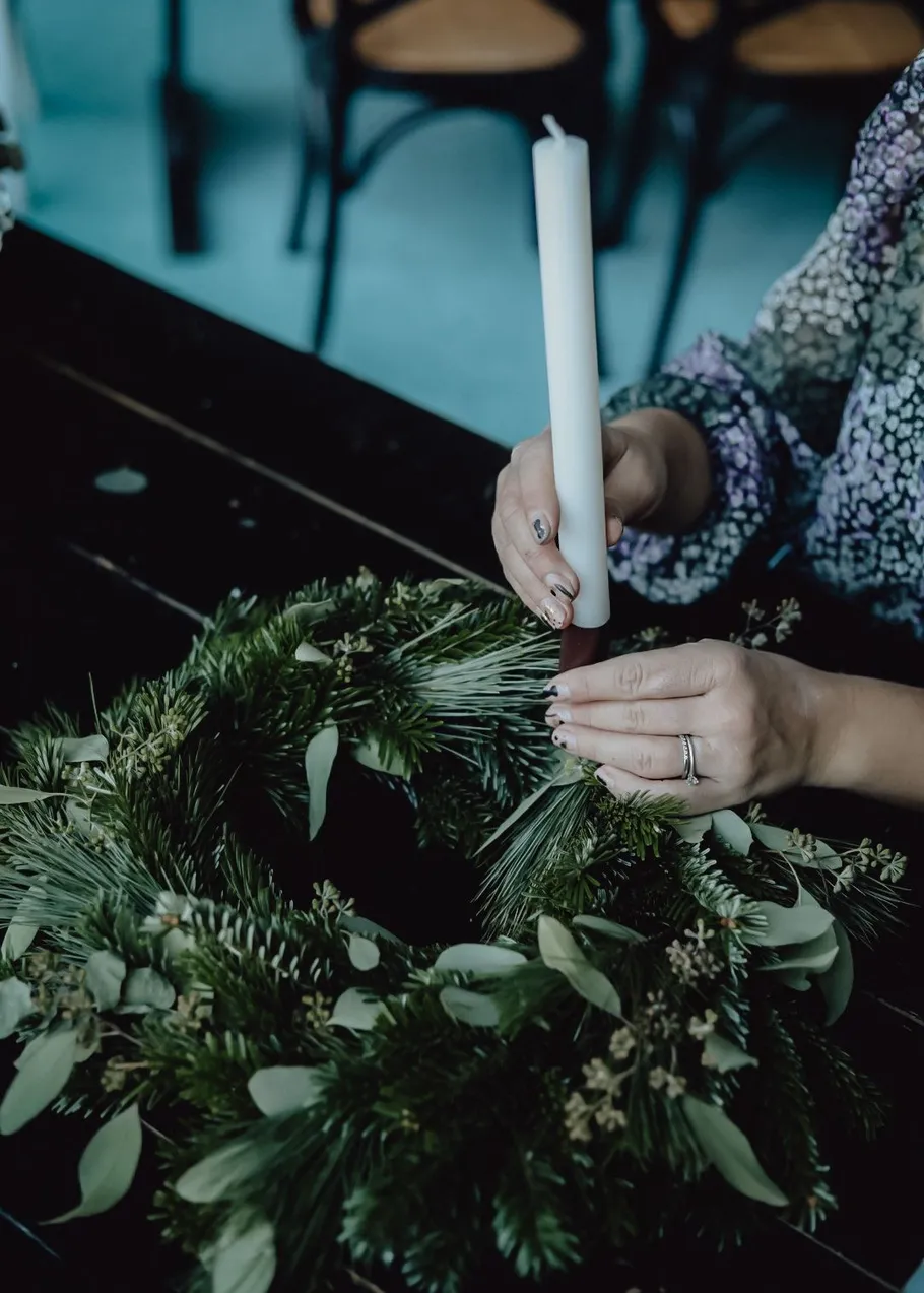 Person arranging candle on festive wreath.
