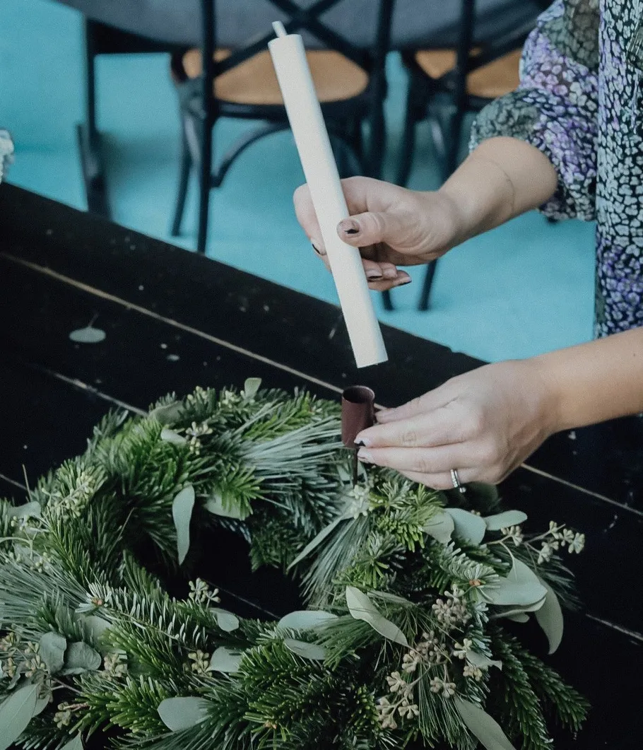 Person places candle on green wreath.