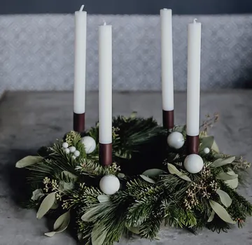 Adventskranz mit vier weißen Kerzen auf Tisch.