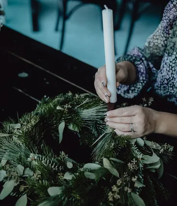Person placing candle on green wreath indoors.