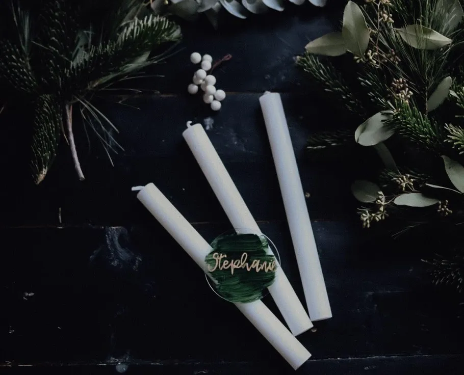 White candles on dark table with foliage.
