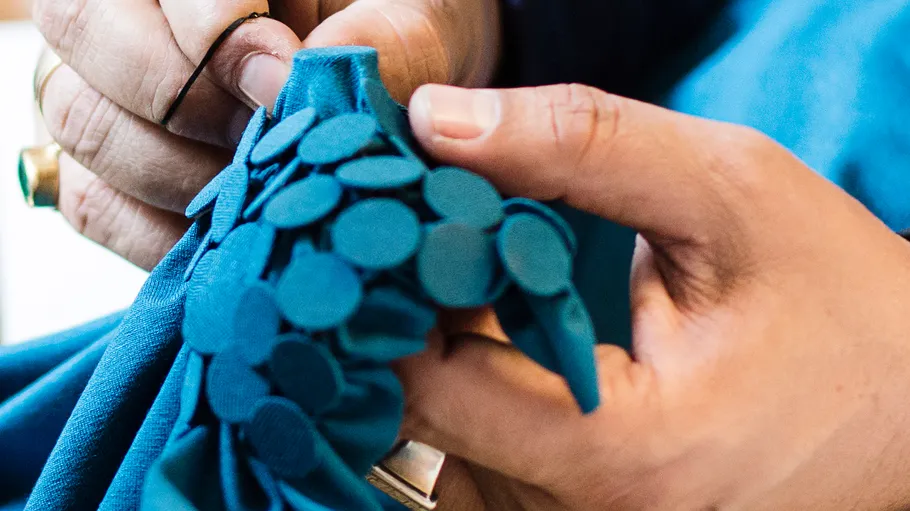 Hands sewing blue fabric with circular designs.