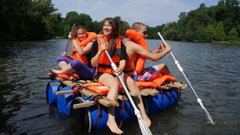 Three people paddling on a homemade raft.