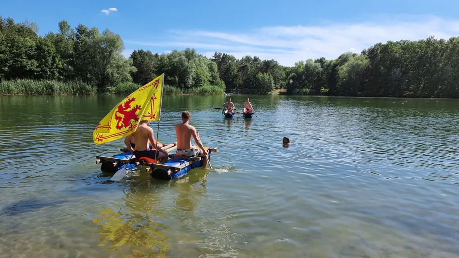 Two people on raft with flag in lake.