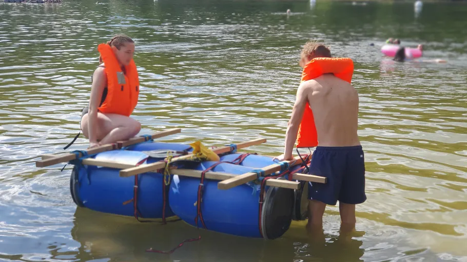 Zwei Personen testen ein selbstgemachtes Floß im Wasser.