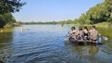Menschen auf Floß paddeln über bewaldeten See.