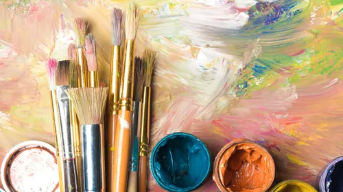 Paintbrushes and paint jars on colorful canvas.