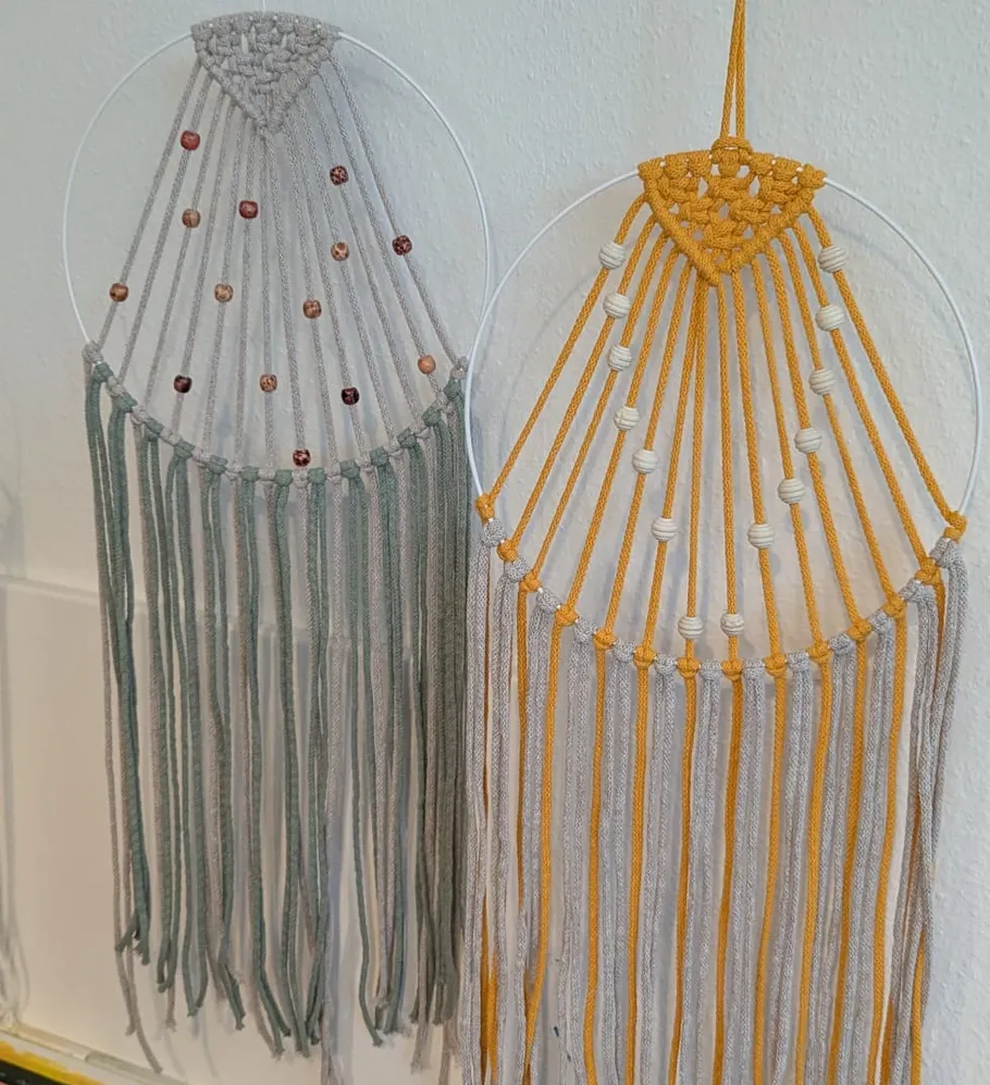 Zwei Makramee-Hänger mit Perlen an einer Wand.