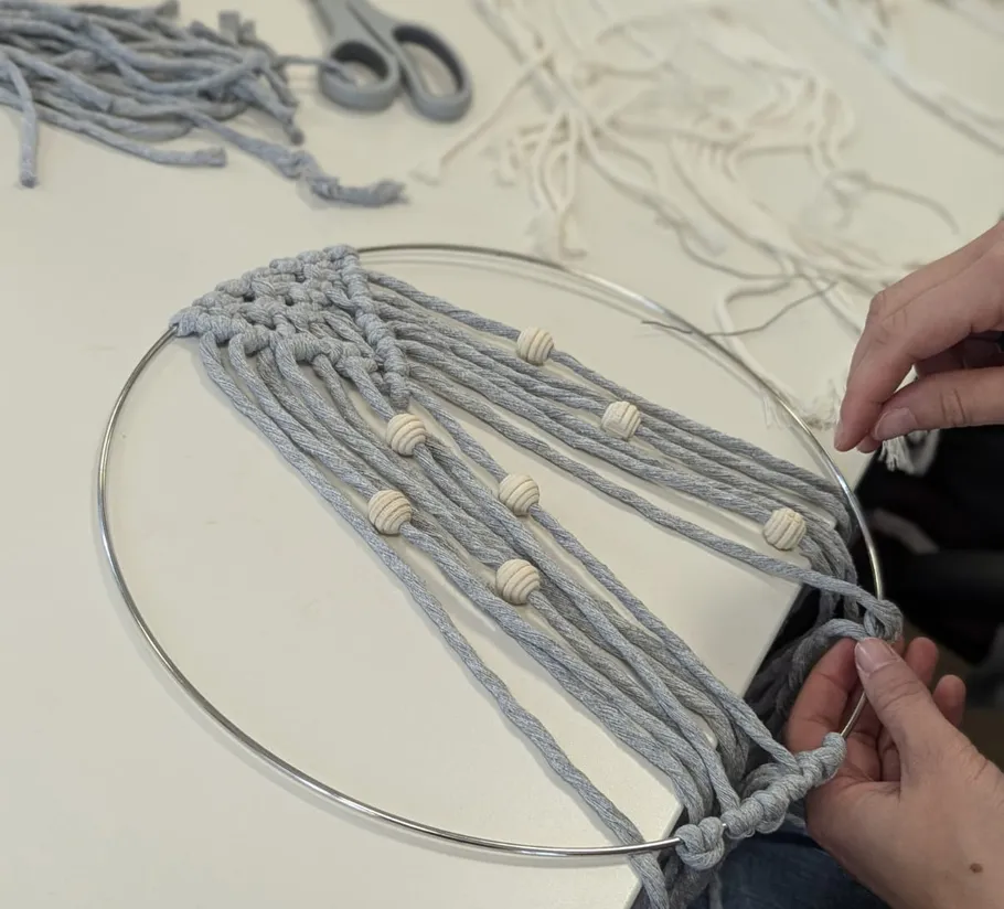 Hands weaving macramé on metal hoop.