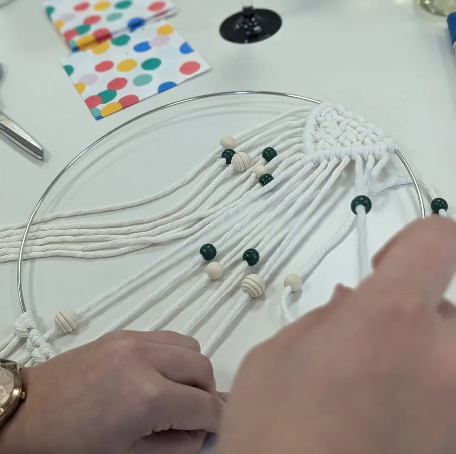 Hands weaving macrame with beads on table.