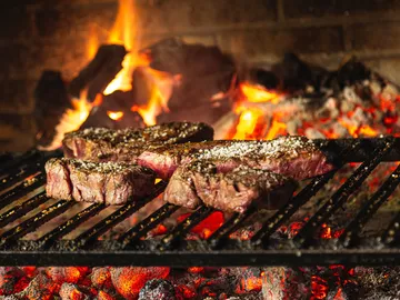 Fleischstücke grillen über glühender Kohle und Flammen.