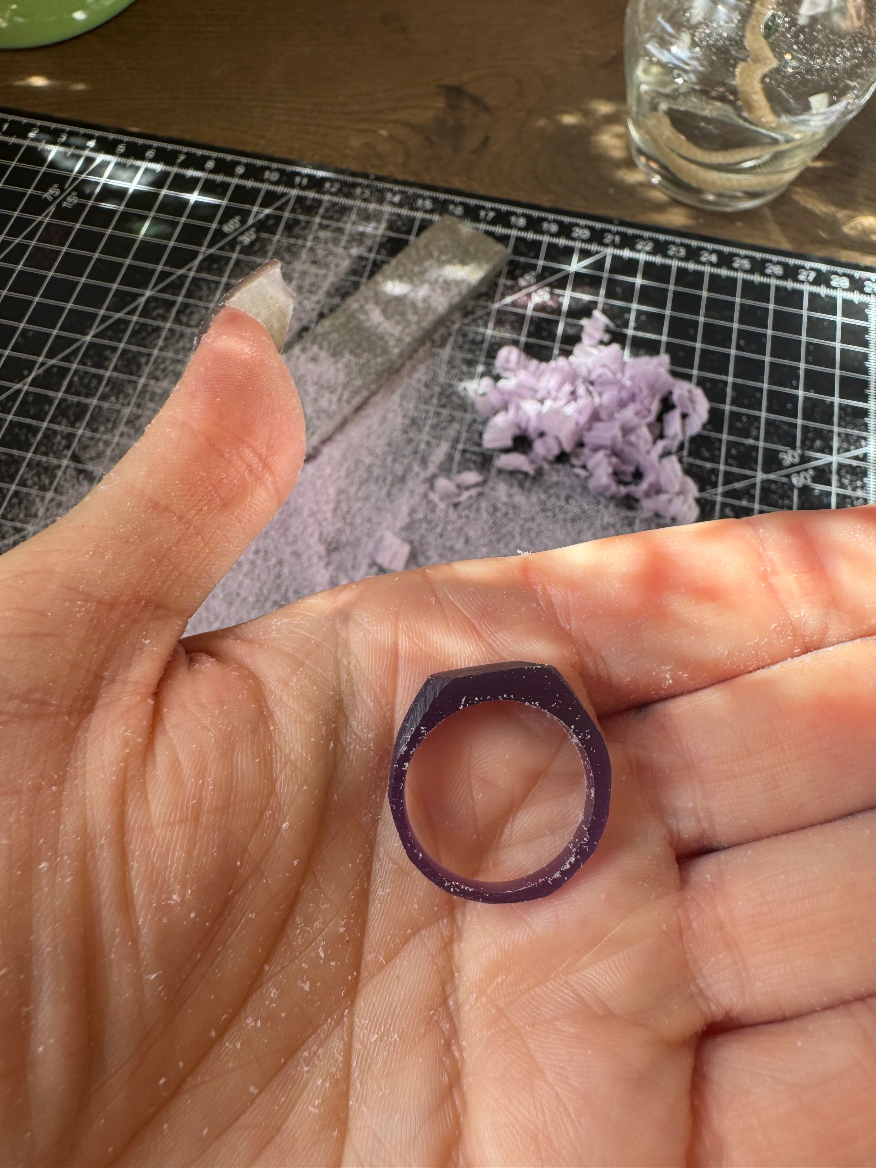 Hand holding a carved ring mold on crafting table.