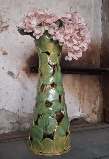 Green vase with pink flowers, rustic background.