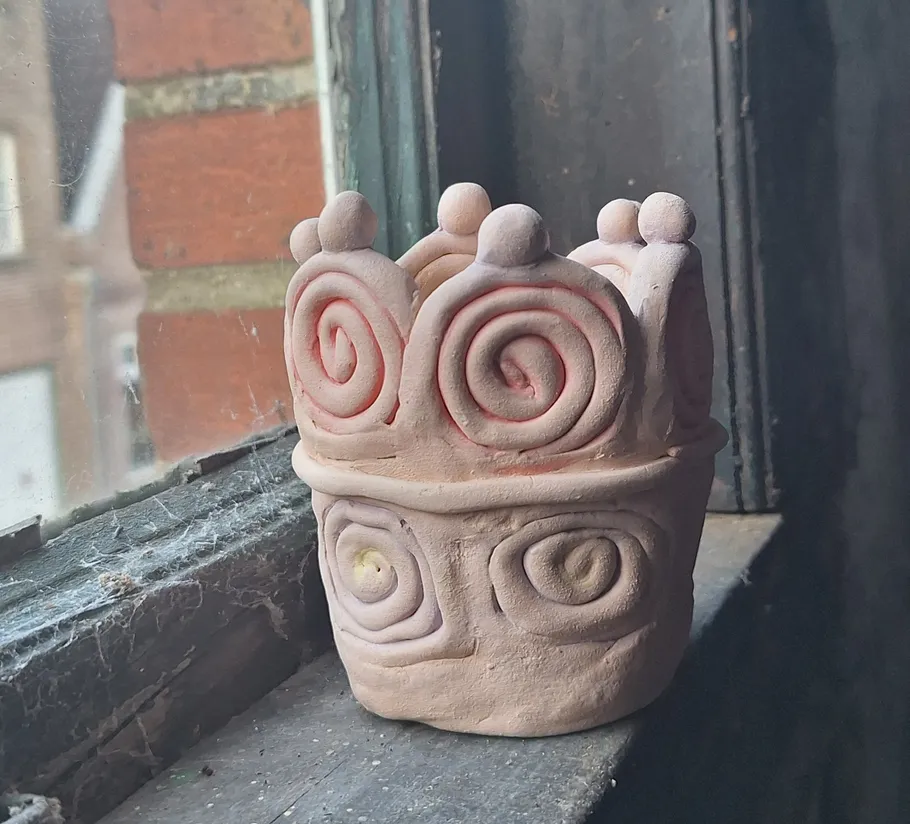 Tontopf mit Spiralmustern auf Fensterbank.