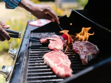 Fleisch wird auf dem Grill gewendet, Flammen lodern auf.