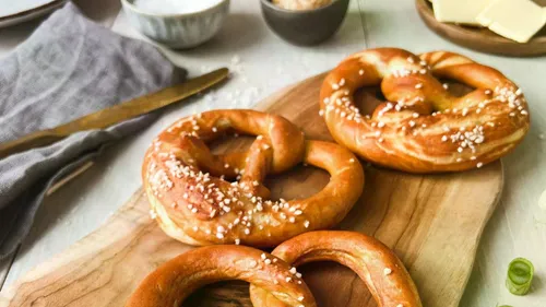 Pretzels on wooden board with condiments nearby.