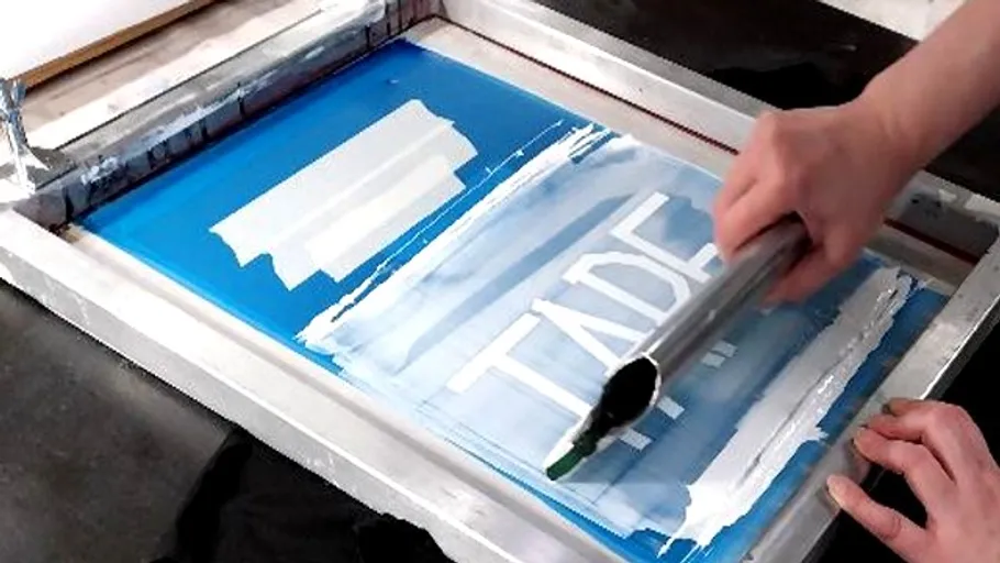 Person beim Siebdrucken auf weißem Stoff, Tinte verteilen.