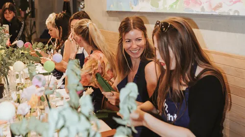 Smiling women crafting with leaves at a table.
