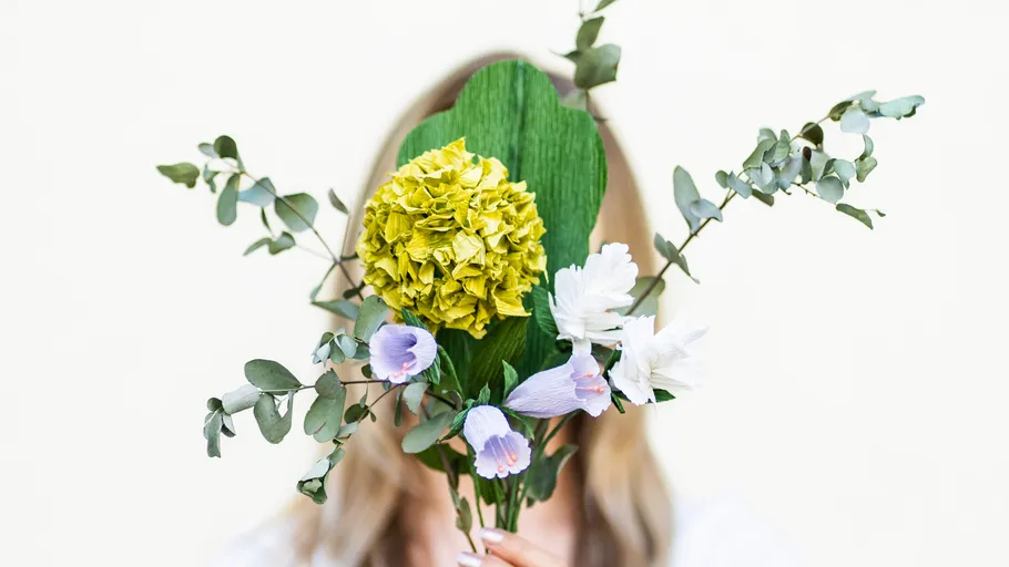 Person holding bouquet covering face, neutral background.