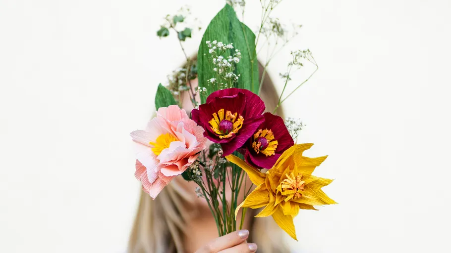 Hand hält bunte Papierblumen.