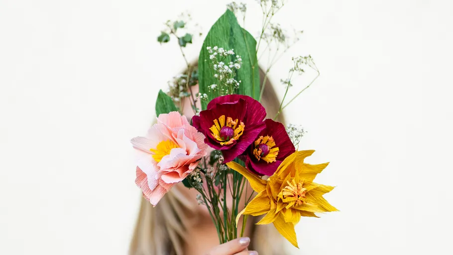 Person hält bunte Blumen, weißer Hintergrund.