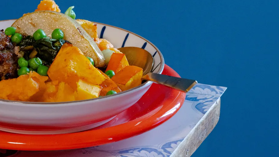 Buntes Gemüsegericht in einer Schüssel, blauer Hintergrund.