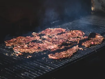 Grilled meat sizzles on a hot grill rack.