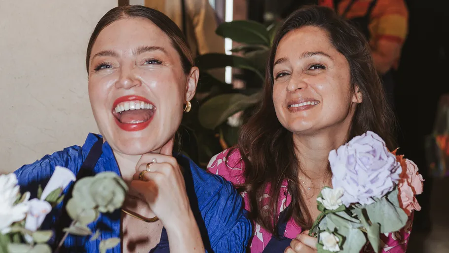 Two smiling women holding flowers indoors.