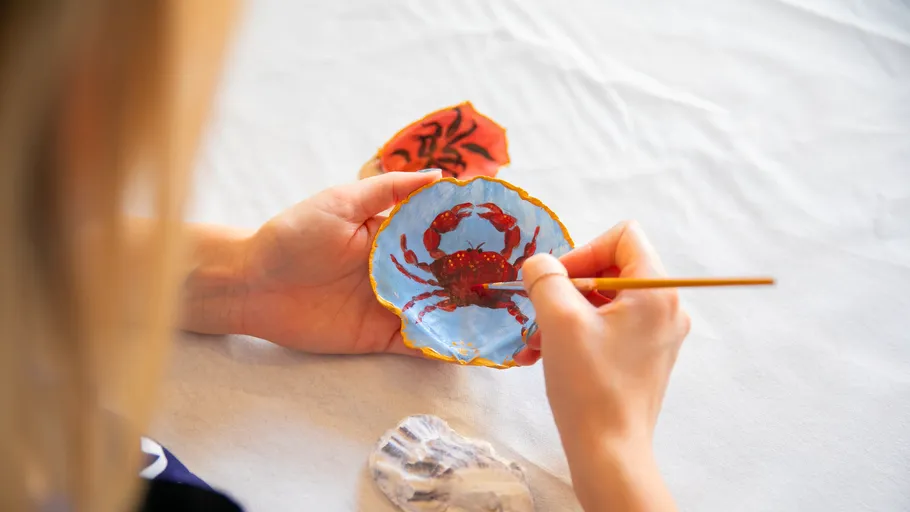 Hand paints crab on shell, table setting.