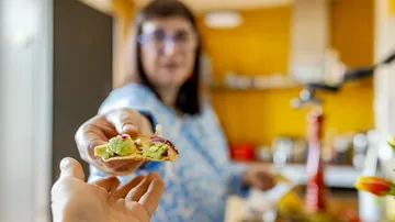 Woman offering a taco in a kitchen.