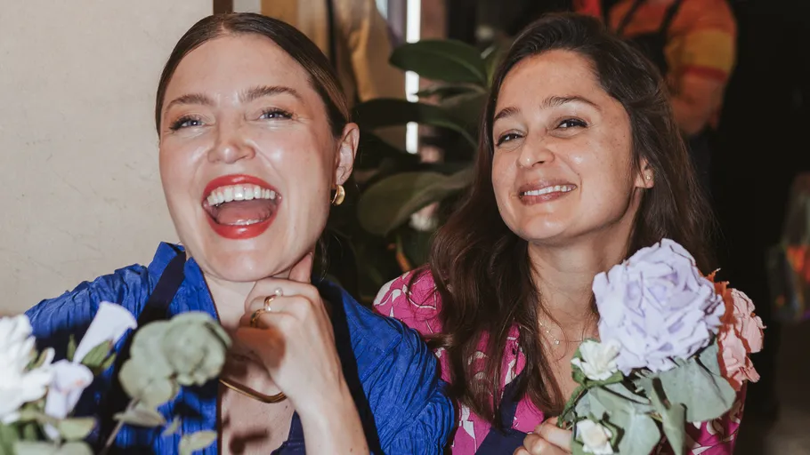 Two women smiling, holding flowers indoors.