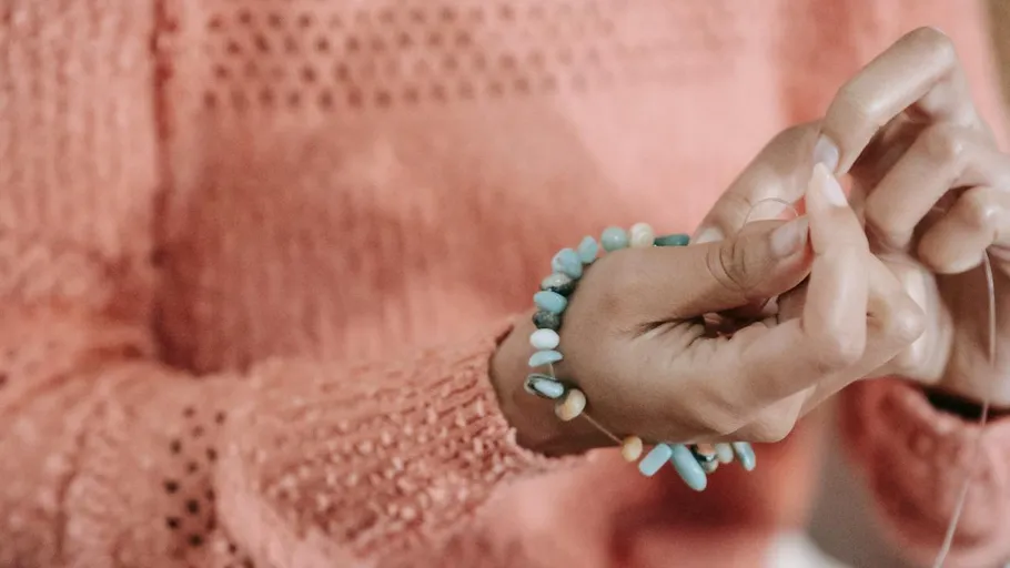 Hands threading beads on a string indoors.