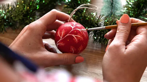 Person painting ornament on wooden table.