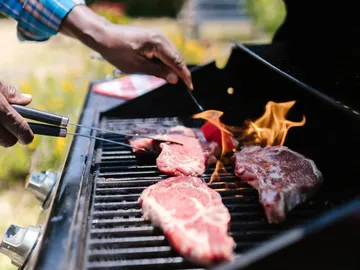 Fleisch brutzelt auf Grill, während Flammen auflodern.